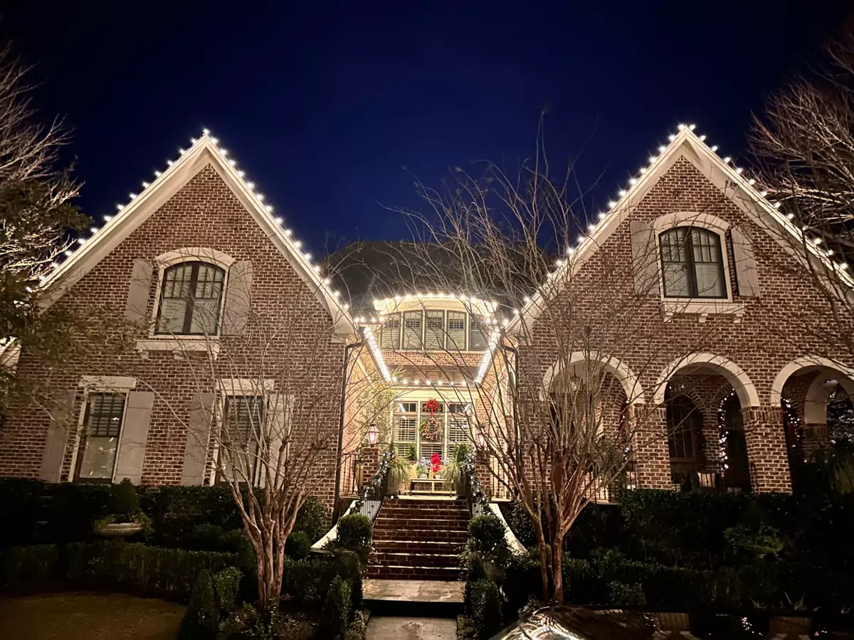 Brick home with twin gables outlined in warm white lights at dusk